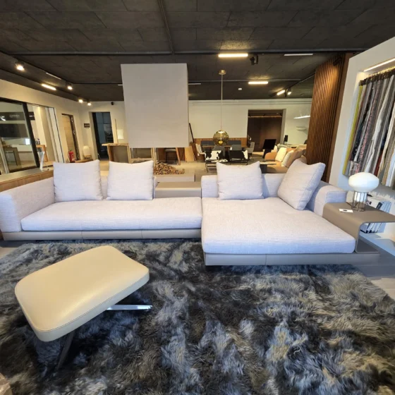 Modernes Minotti Connery Sofa mit hellgrauem Stoffbezug und integriertem Beistelltisch im Möbelstudio mit Teppich und