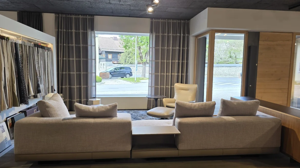 Moderner Showroom mit Minotti Connery Sofa in hellgrauem Stoff, beiger Leder-Sessel mit Hocker, Vorhängen und Holzfußboden