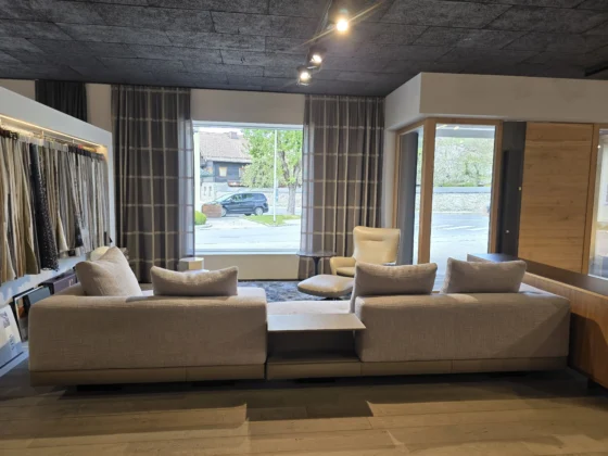 Moderner Showroom mit Minotti Connery Sofa in hellgrauem Stoff, beiger Leder-Sessel mit Hocker, Vorhängen und Holzfußboden