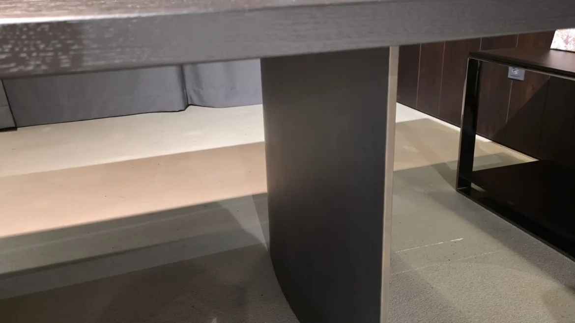 Moderner Minotti Linha Tisch mit dunkler Holzplatte und zentralem Metallfuß in elegantem Showroom-Interieur