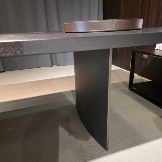 Moderner Minotti Linha Tisch mit dunkler Holzplatte und zentralem Metallfuß in elegantem Showroom-Interieur