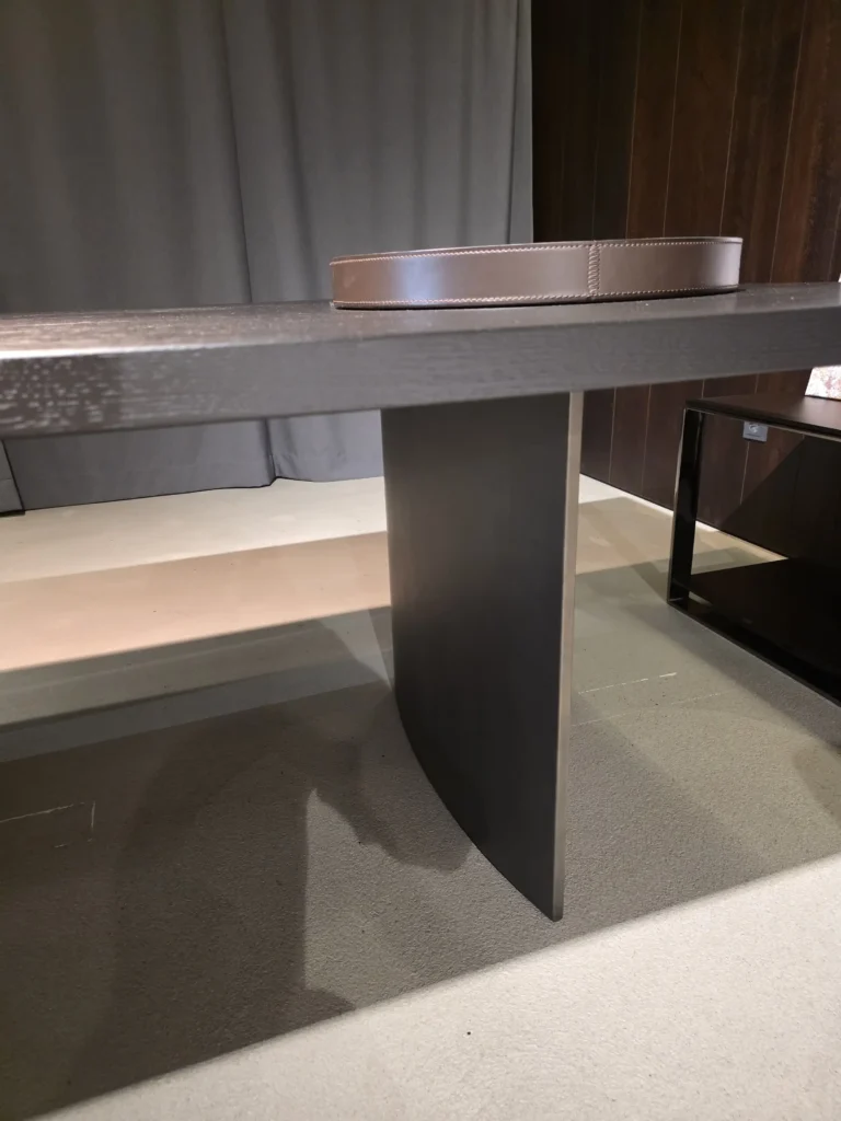 Moderner Minotti Linha Tisch mit dunkler Holzplatte und zentralem Metallfuß in elegantem Showroom-Interieur