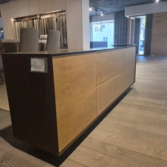 Moderner Holz- und Metall-Sideboard im Möbelstudio mit Stühlen und Stoffmustern im Hintergrund