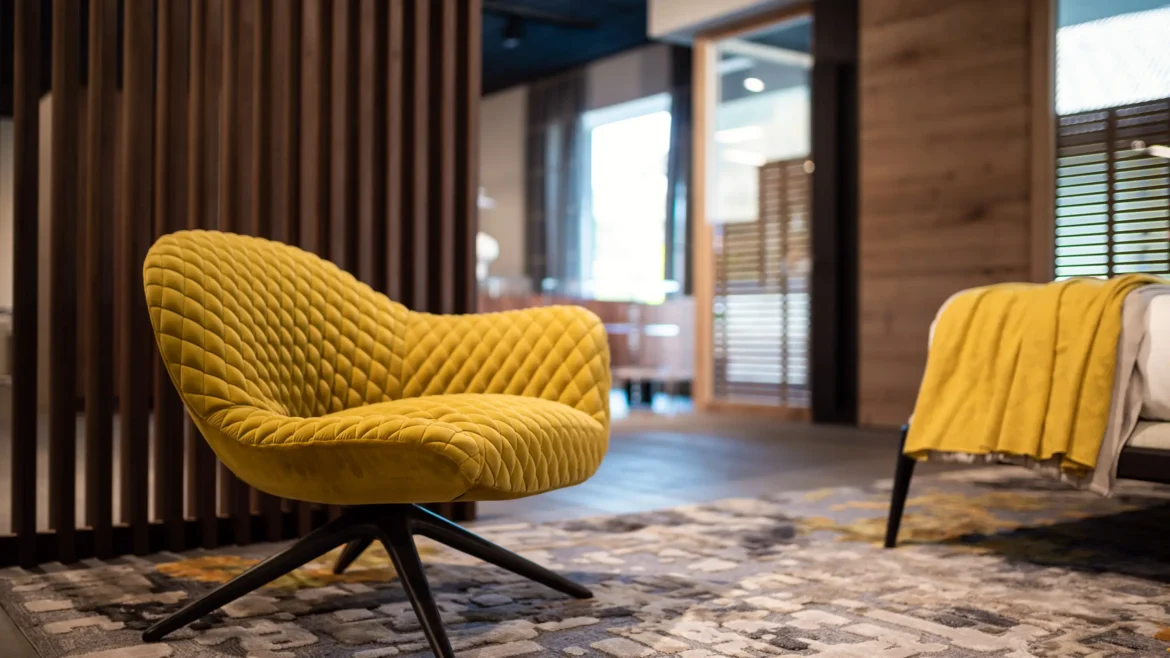 Gelber, gepolsterter Design-Sessel auf gemustertem Teppich vor Holzlamellen in modernem Möbelstudio