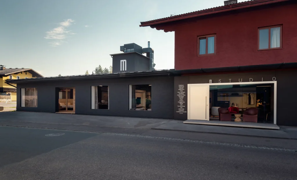 Moderner Showroom mit großen Fenstern, schwarzer Fassade und sichtbaren Designermöbeln im Innenraum, M Studio Schriftzug