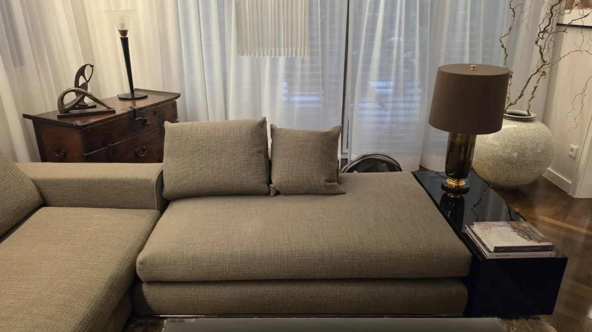 Beiges Minotti Hamilton Sofa mit zwei Kissen, schwarzer Beistelltisch mit Lampe und Bücher im modernen Wohnzimmer mit