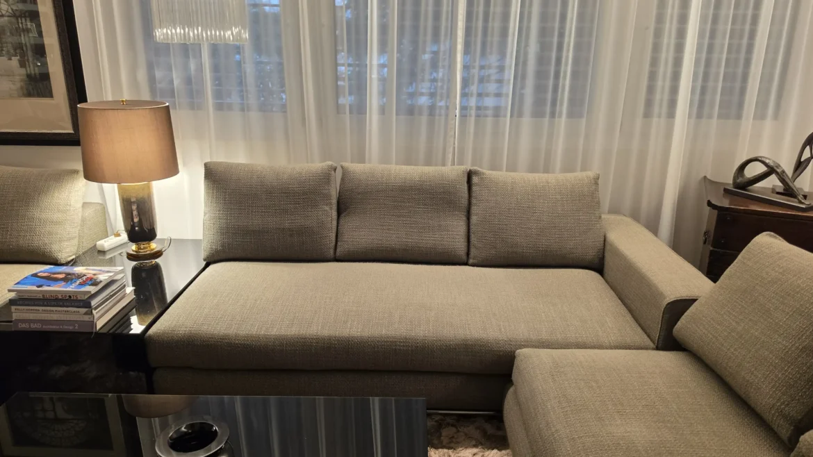 Beige Minotti Hamilton Sofa in modernem Wohnzimmer mit Tisch, Lampe und Vorhängen im Möbelstudio Showroom.