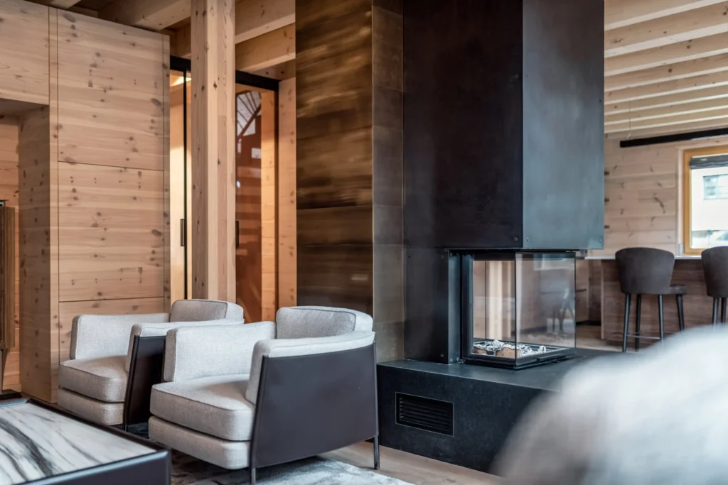 Moderner Wohnraum mit zwei grauen Sesseln, schwarzem Kamin und Holzverkleidung, stilvolle Innenarchitektur und Möbelstudio